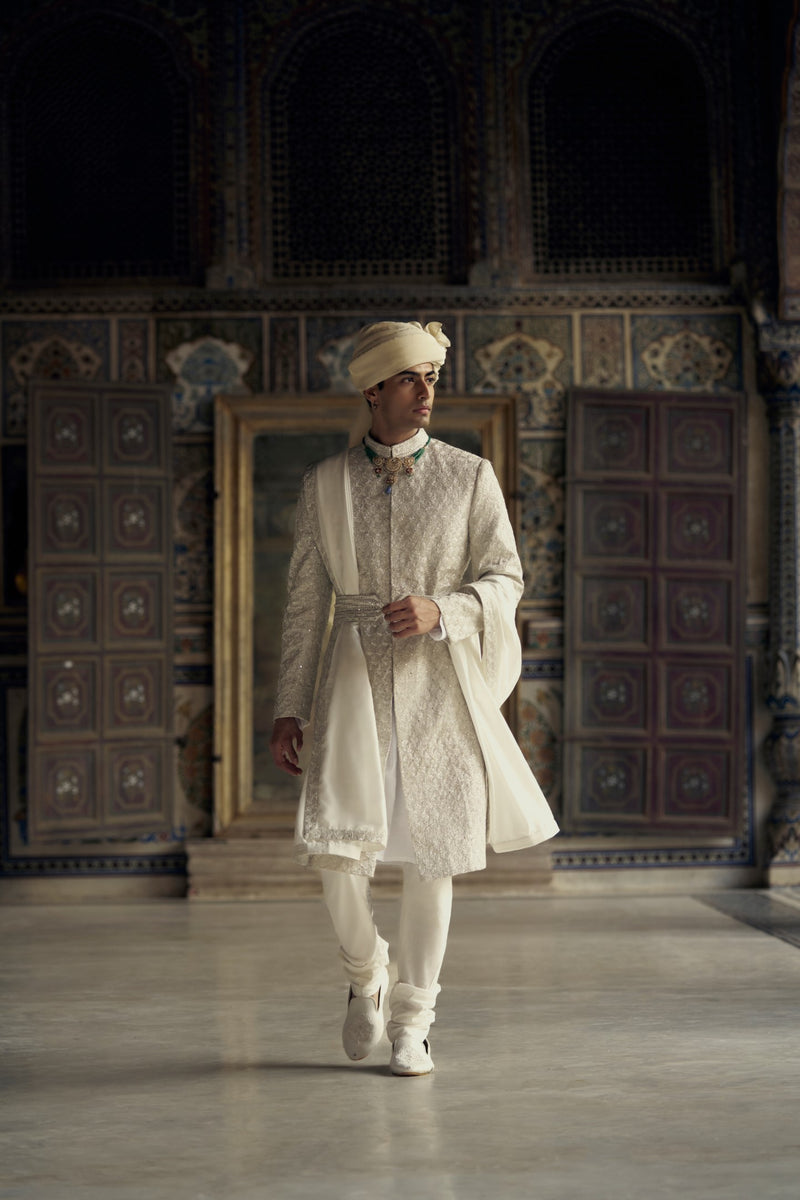 IVORY RAW SILK SHERWANI WITH KURTA AND CHURIDAR WITH AN OPTIONAL WORKED STOLE AND BELT AND EMBROIDERED JUTIS.