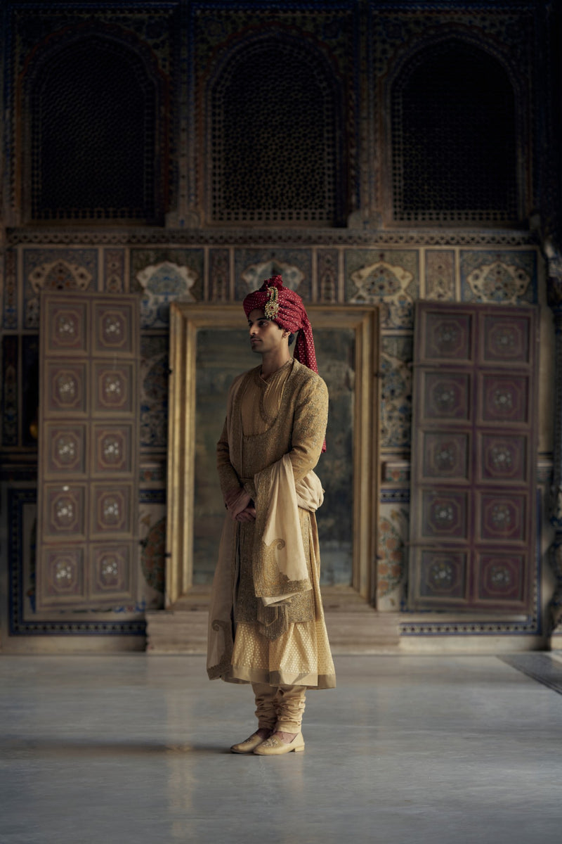 GOLD MATKA SILK ANGRAKHA STYLE SHERWANI WITH A CHANDERI BOOTI CHOGA AND CHURIDAR. IT HAS AN OPTIONAL BELT , STOLE AND WORKED JUTIS