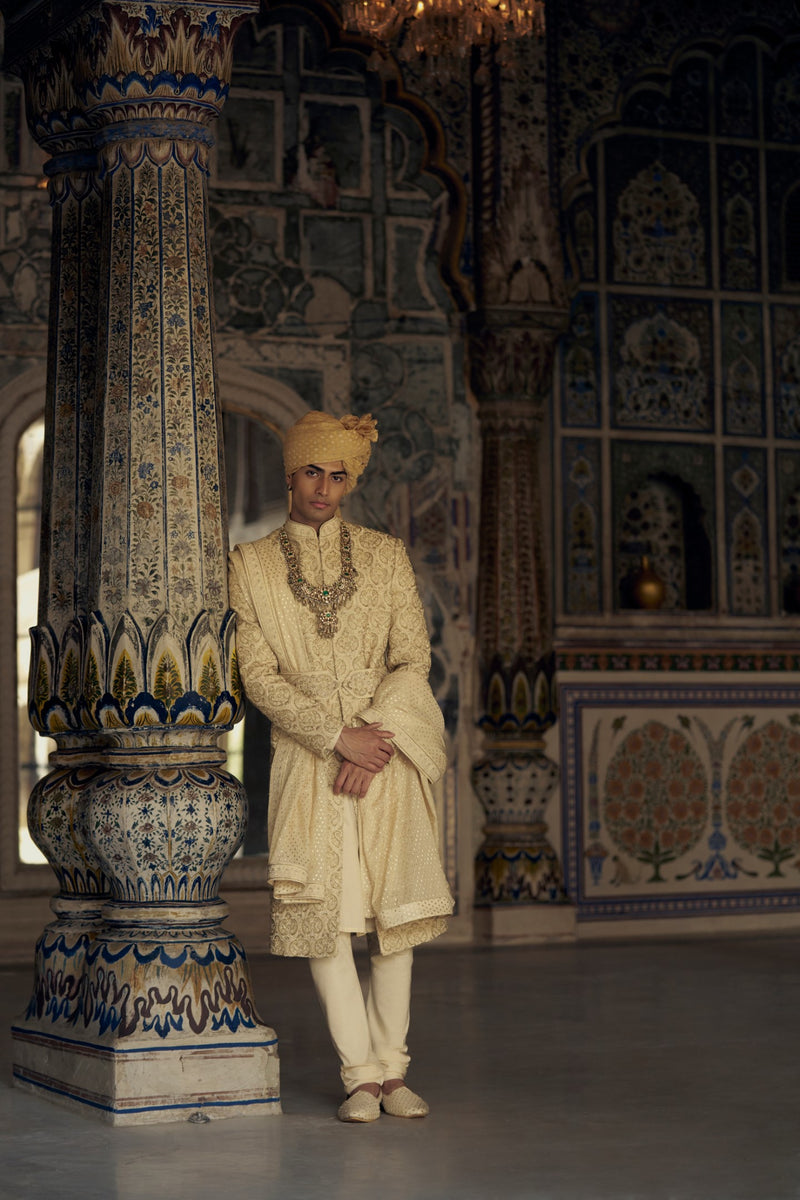 GOLD RAW SILK SHERWANI WITH KURTA AND CHURIDAR WITH AN OPTIONAL WORKED BELT, STOLE AND JUTIS.