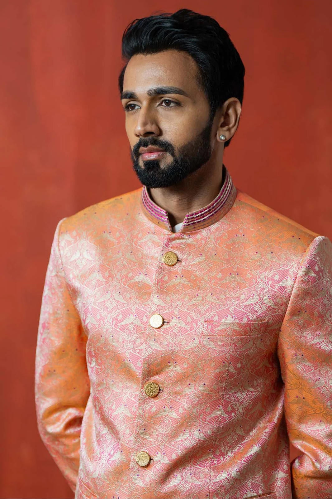 Man wearing a traditional pink sherwani against a red background
