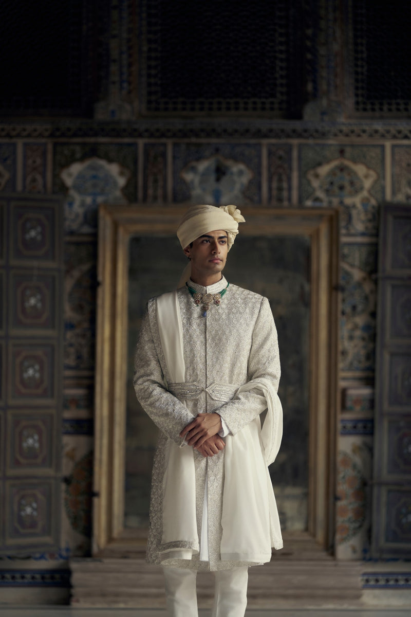 IVORY RAW SILK SHERWANI WITH KURTA AND CHURIDAR WITH AN OPTIONAL WORKED STOLE AND BELT AND EMBROIDERED JUTIS.