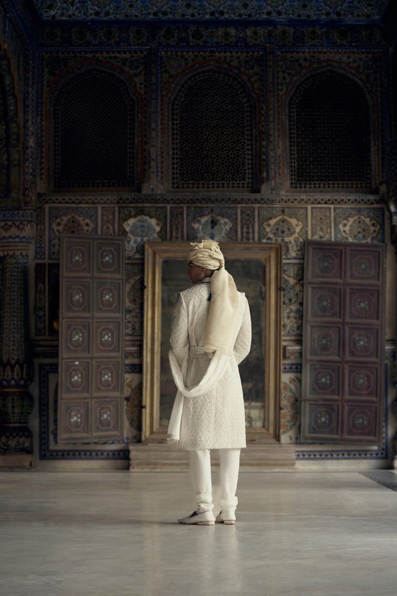 IVORY RAW SILK SHERWANI WITH KURTA AND CHURIDAR WITH AN OPTIONAL WORKED STOLE AND BELT AND EMBROIDERED JUTIS.