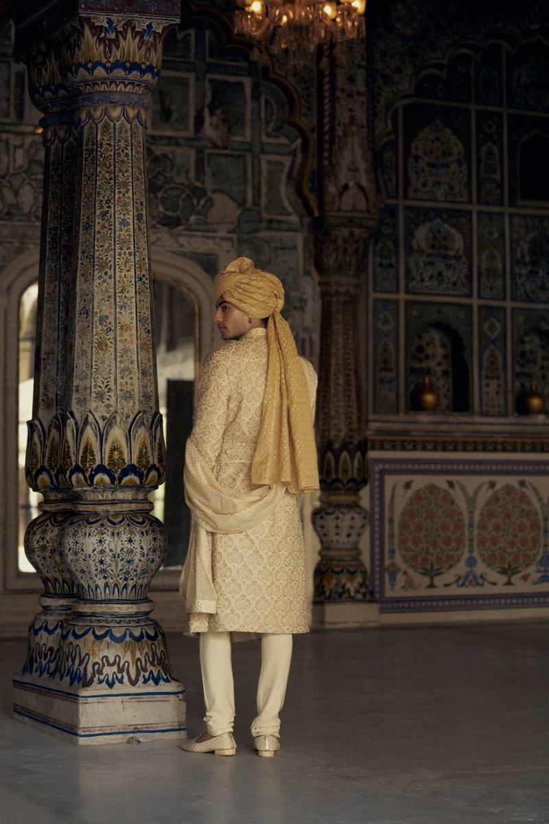 GOLD RAW SILK SHERWANI WITH KURTA AND CHURIDAR WITH AN OPTIONAL WORKED BELT, STOLE AND JUTIS.