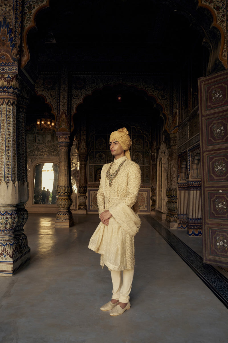 GOLD RAW SILK SHERWANI WITH KURTA AND CHURIDAR WITH AN OPTIONAL WORKED BELT, STOLE AND JUTIS.